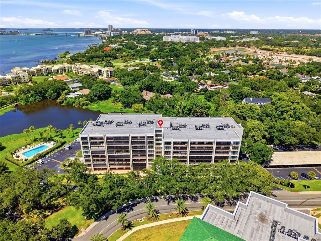 An aerial view shows a multi-story apartment building surrounded by trees, a pond, and parking — 220 BELLEVIEW BOULEVARD UNIT 207, BELLEAIR, FL