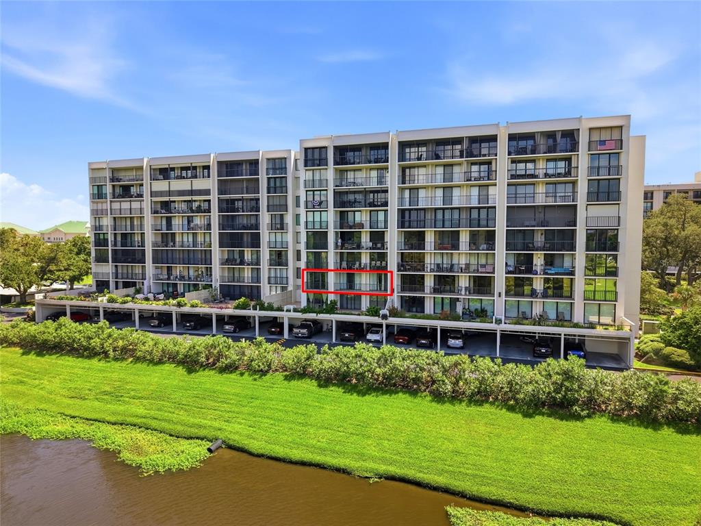 An exterior view of a multi-story apartment building with a red-outlined balcony overlooking a pond — 220 BELLEVIEW BOULEVARD UNIT 207, BELLEAIR, FL