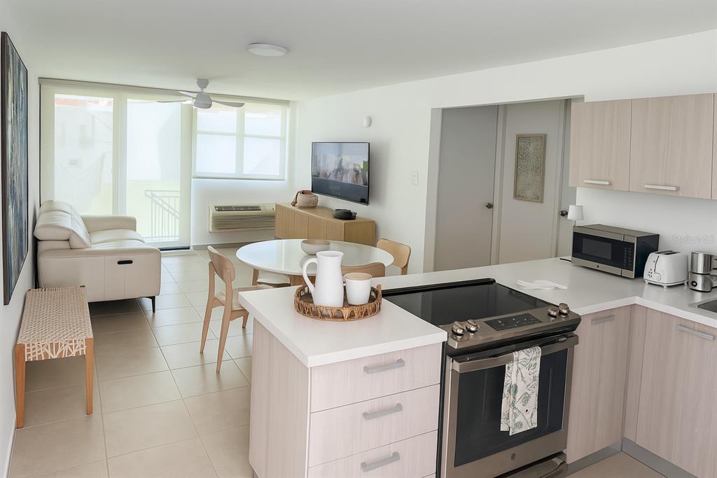 An open-concept living and kitchen area features light wood cabinets, white countertops, and tile flooring — C-116 MARBELA CASA DE PLAYA UNIT 1, ISABELA, PR