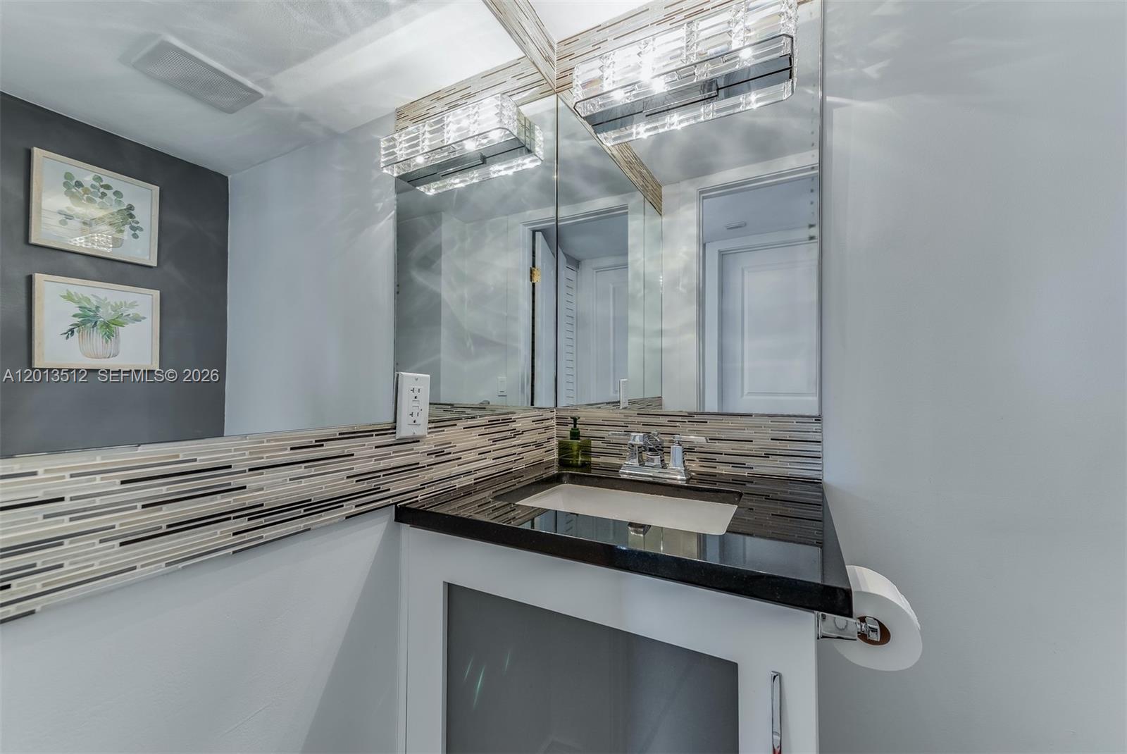 A bathroom features a black countertop, white vanity, mosaic tile backsplash, and a large mirror — 200 178th Dr # 604, Sunny Isles Beach FL 33160, SUNNY ISLES BEACH, FL