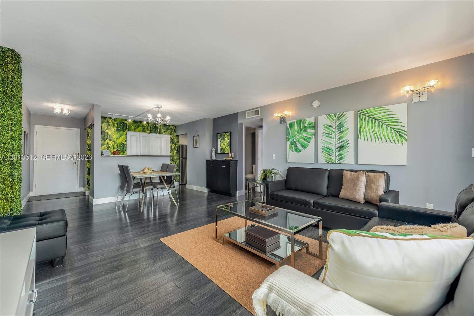 A living room and dining area feature dark wood floors, black furniture, and tropical decor — 200 178th Dr # 604, Sunny Isles Beach FL 33160, SUNNY ISLES BEACH, FL