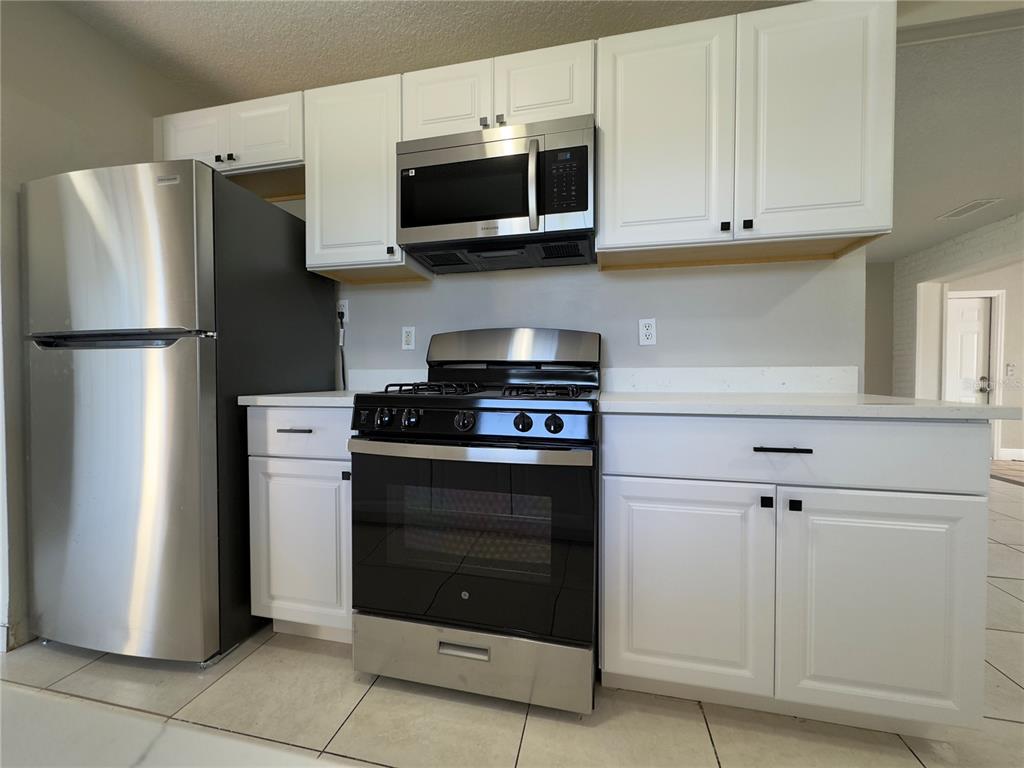 A kitchen features white cabinets, stainless steel appliances, and light-colored tile flooring — 1219 BROWNING AVENUE, ORLANDO, FL