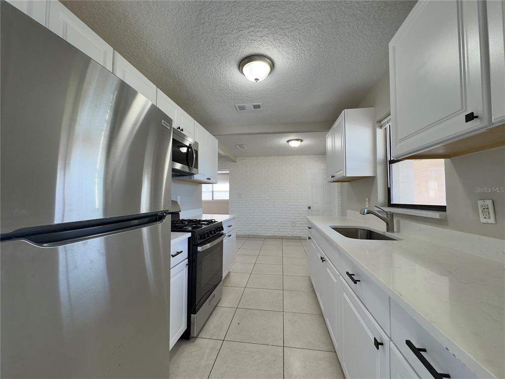A kitchen features white cabinets, stainless steel appliances, light countertops, and tile flooring — 1219 BROWNING AVENUE, ORLANDO, FL
