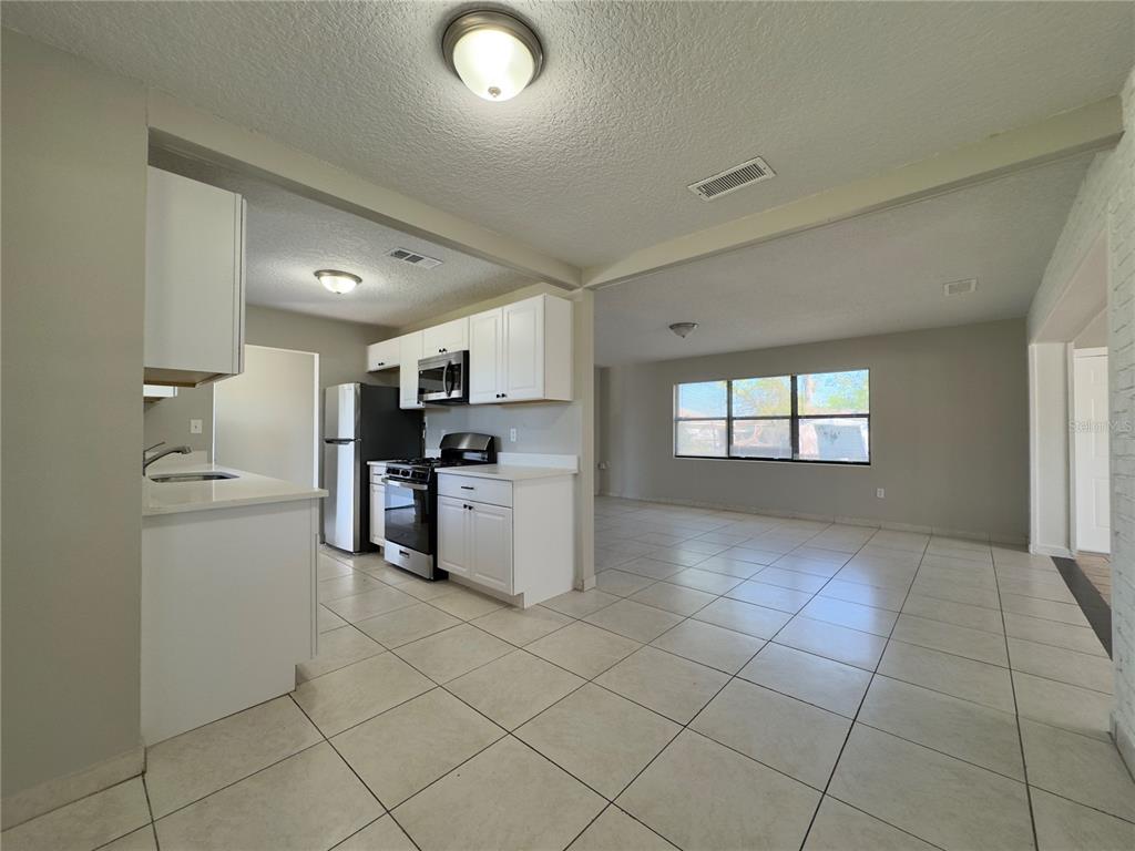 A kitchen with white cabinets and tile flooring opens into a spacious, sunlit living area — 1219 BROWNING AVENUE, ORLANDO, FL