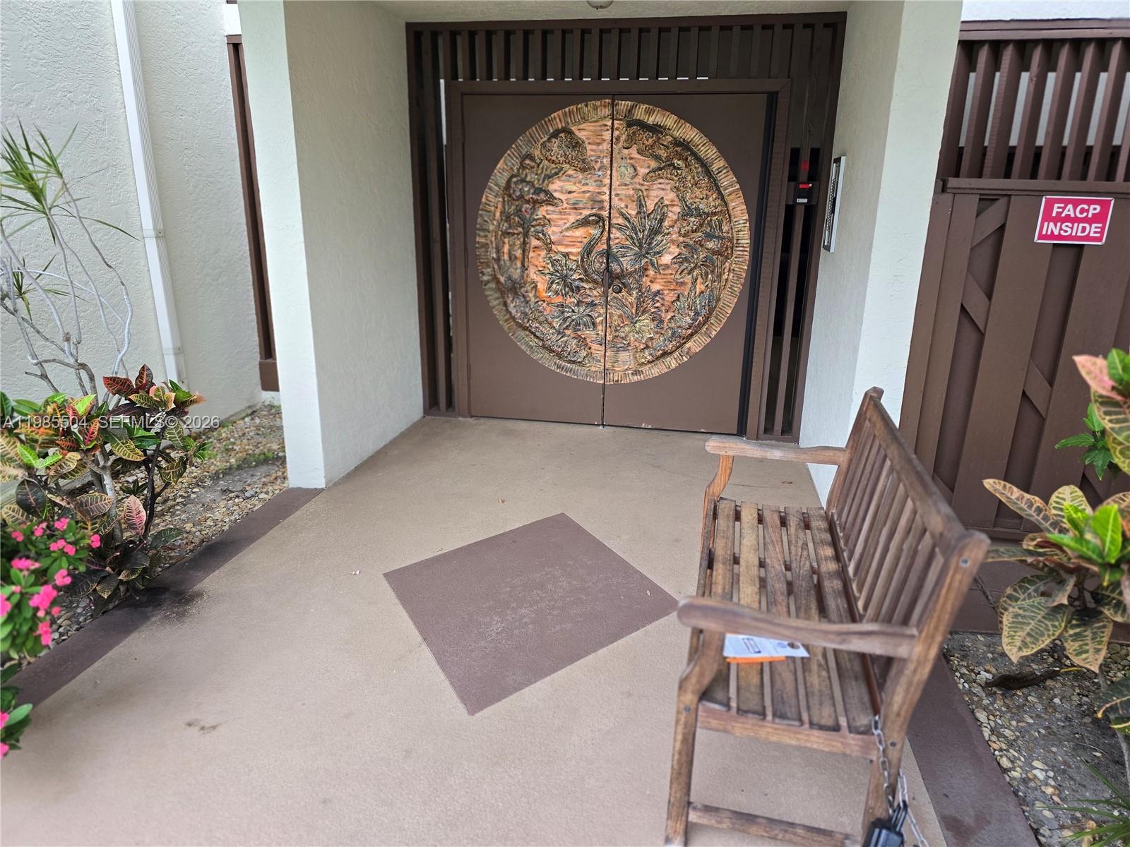 A wooden bench sits on a patio in front of double doors with decorative carvings — 166 SE St Lucie Blvd # Un # 203, Stuart FL 34996, STUART, FL