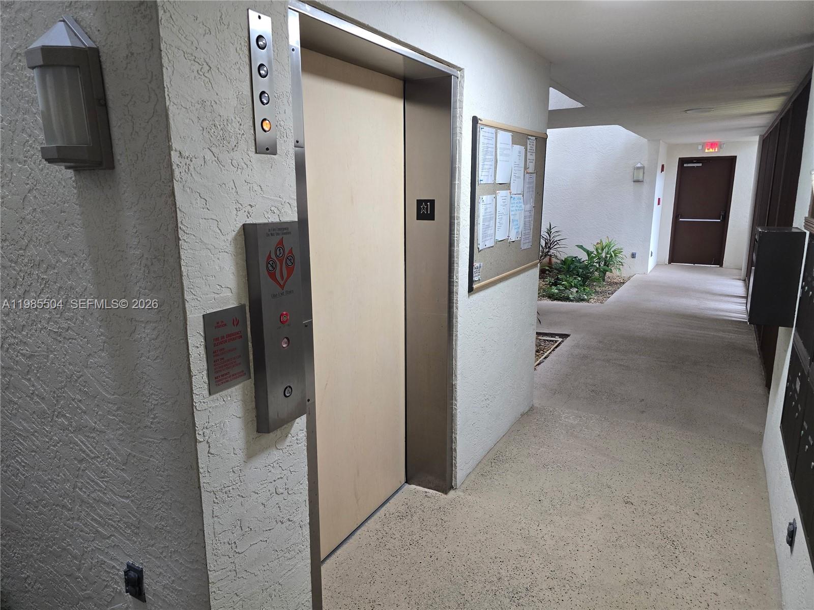 An elevator door is located in a hallway with a bulletin board and outdoor plants — 166 SE St Lucie Blvd # Un # 203, Stuart FL 34996, STUART, FL