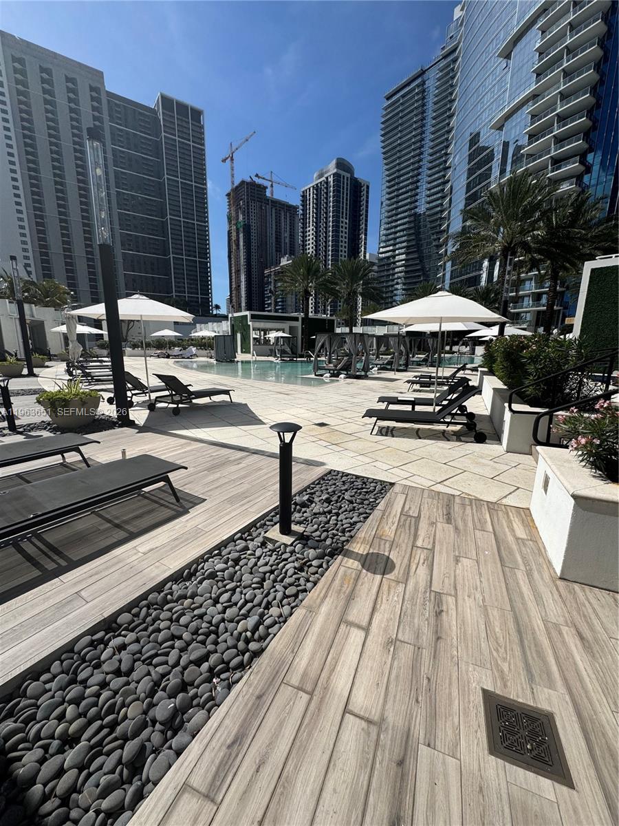 An outdoor swimming pool area features lounge chairs, umbrellas, and modern high-rise buildings — 851 NE 1st ave # 7, Miami FL 33132, MIAMI, FL