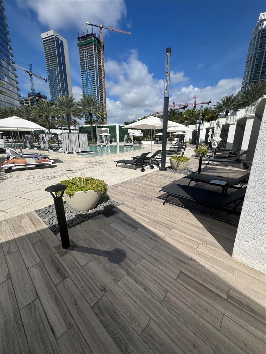 An outdoor pool deck features lounge chairs, umbrellas, planters, and tall residential buildings under construction — 851 NE 1st ave # 7, Miami FL 33132, MIAMI, FL