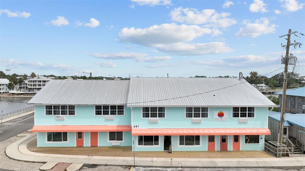 A two-story, light blue building with a metal roof and coral-colored awnings sits waterfront — 491 DOCK STREET, CEDAR KEY, FL