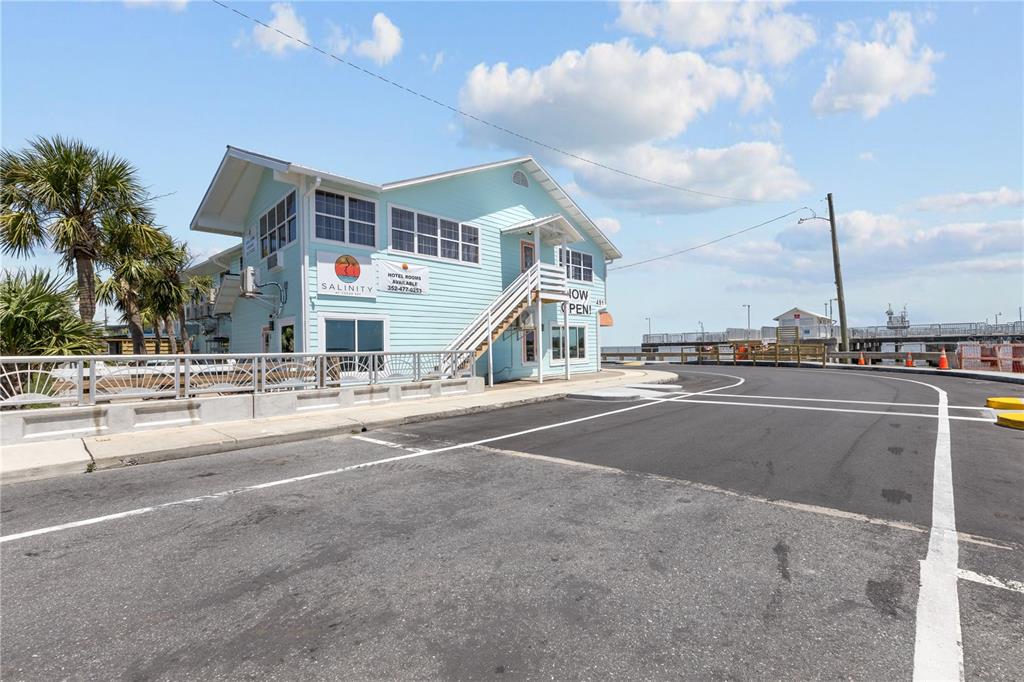 A light blue, two-story building with a staircase stands next to an asphalt road — 491 DOCK STREET, CEDAR KEY, FL