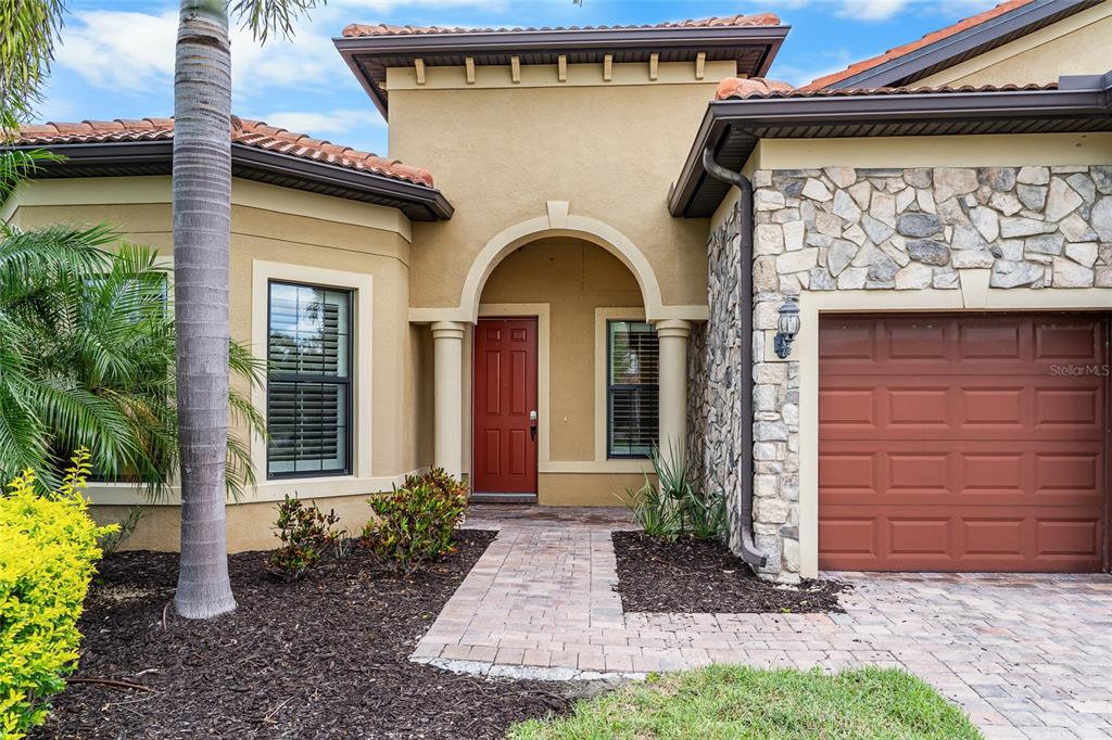 A single-story house exterior features a red front door, stone facade, and a paved walkway — 5700 SWEET LEAF WAY, SARASOTA, FL