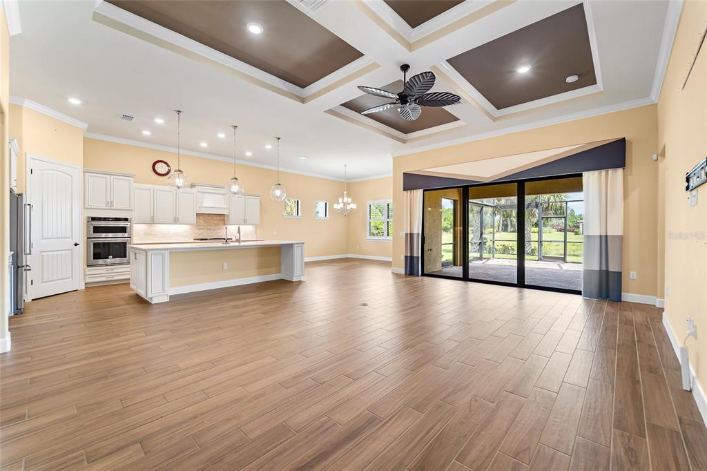 A spacious kitchen and living area features a coffered ceiling, wood-look tile, and sliding doors — 5700 SWEET LEAF WAY, SARASOTA, FL
