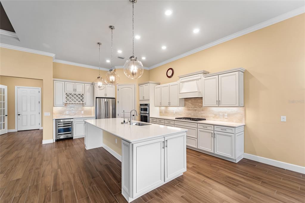 A modern kitchen features white cabinetry, a large central island, and wood-look tile flooring — 5700 SWEET LEAF WAY, SARASOTA, FL