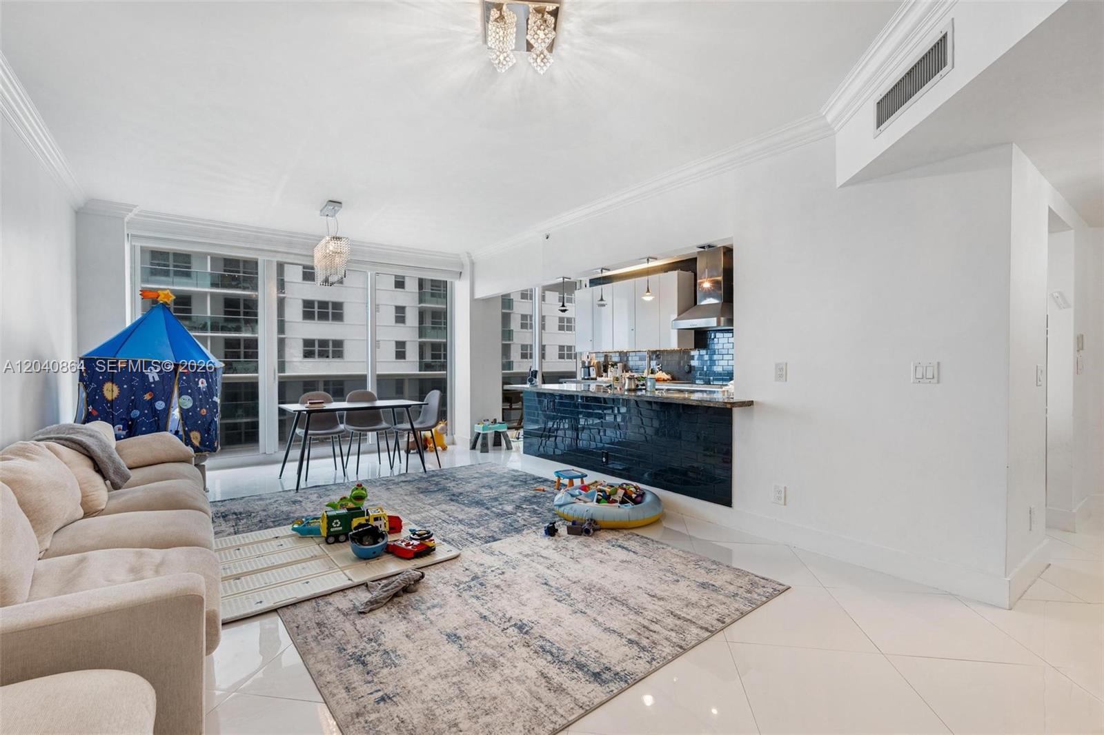 A living room and kitchen area with white walls, tile floors, and a blue backsplash — 9559 Collins Ave # J, Surfside FL 33154, SURFSIDE, FL