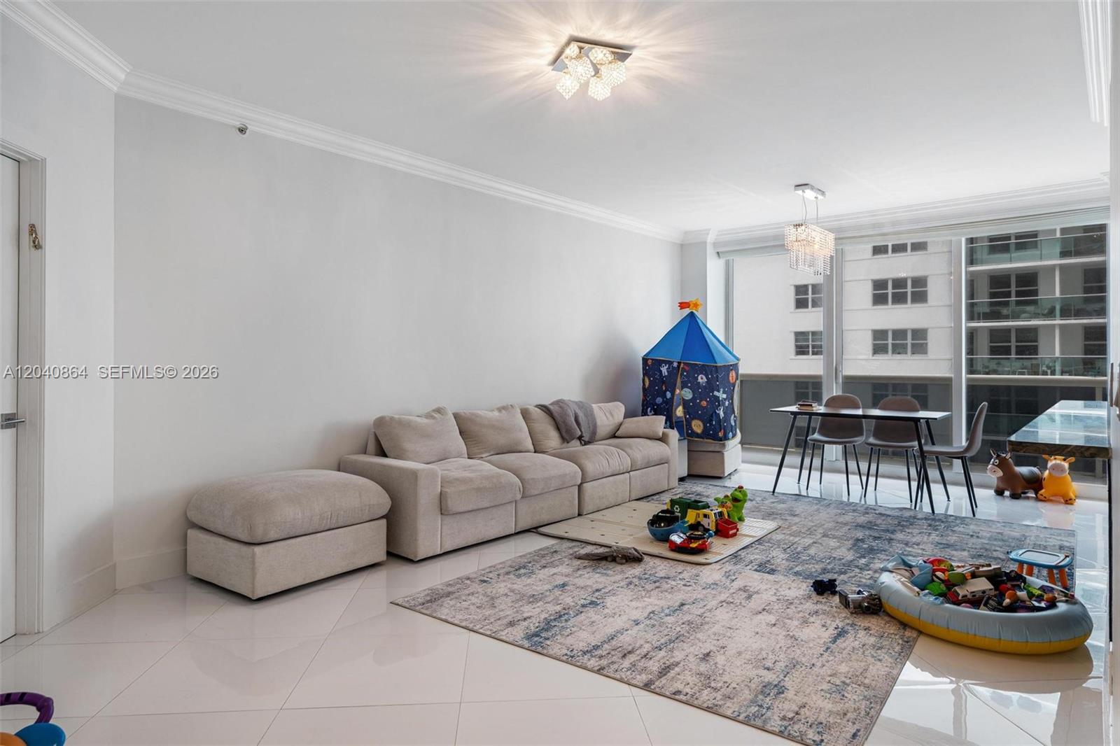 A living room with a beige sofa, area rug, dining table, and children's play items — 9559 Collins Ave # J, Surfside FL 33154, SURFSIDE, FL