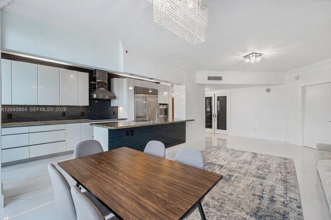 A modern kitchen with white cabinets and a dark tile island overlooks a dining area — 9559 Collins Ave # J, Surfside FL 33154, SURFSIDE, FL