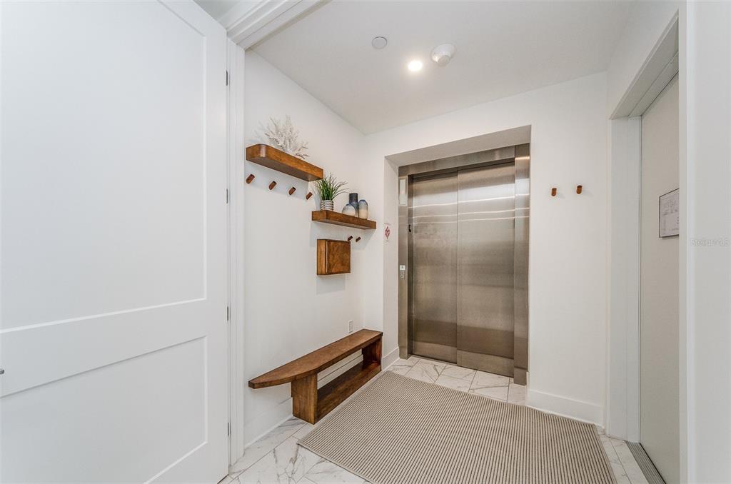 An entryway features a wooden bench, wall-mounted shelves, and a stainless steel elevator door — 15 AVALON STREET UNIT 401, CLEARWATER BEACH, FL