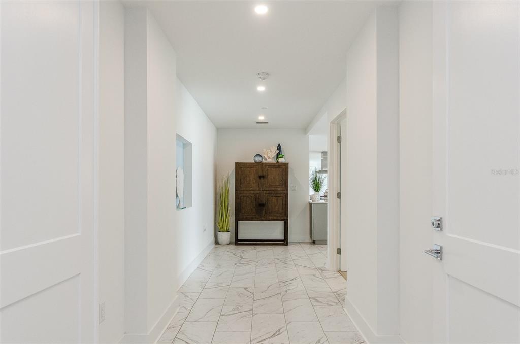 A bright hallway features white walls, marble-look tile flooring, and a dark wooden cabinet — 15 AVALON STREET UNIT 401, CLEARWATER BEACH, FL