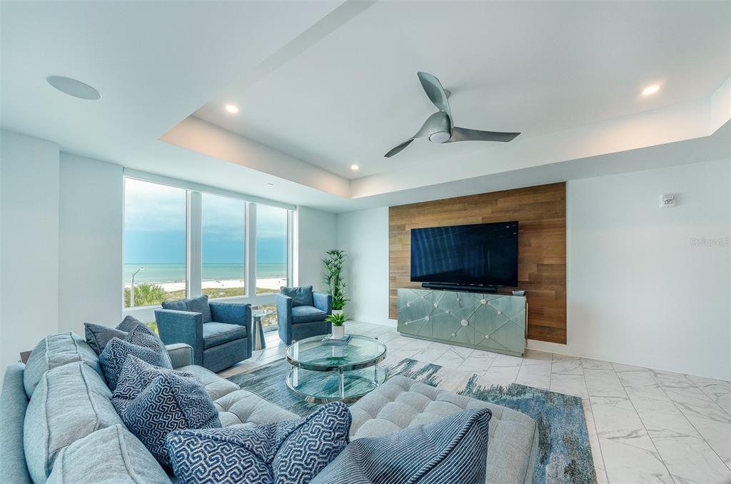 A modern living room features a gray sectional, blue armchairs, and a wood-paneled TV wall — 15 AVALON STREET UNIT 401, CLEARWATER BEACH, FL