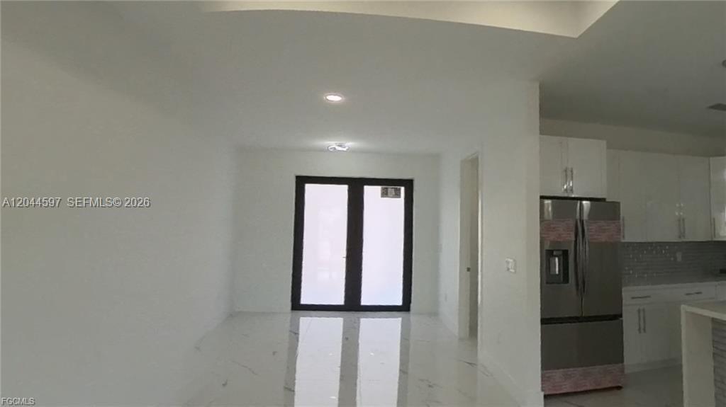 A bright, open-concept room features white marble-style flooring, white cabinetry, and a stainless steel refrigerator — 3004 SW 4TH ST, Lehigh Acres FL 33976, LEHIGH ACRES, FL