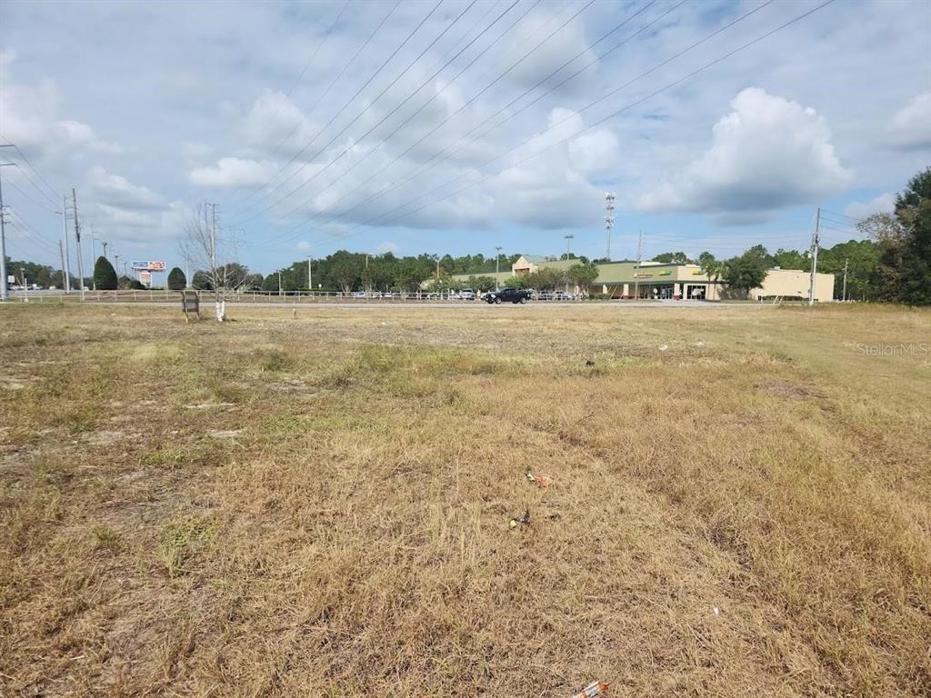 A vacant, grassy lot sits in front of a commercial shopping center under a cloudy sky — 7013 SE MARICAMP ROAD, OCALA, FL
