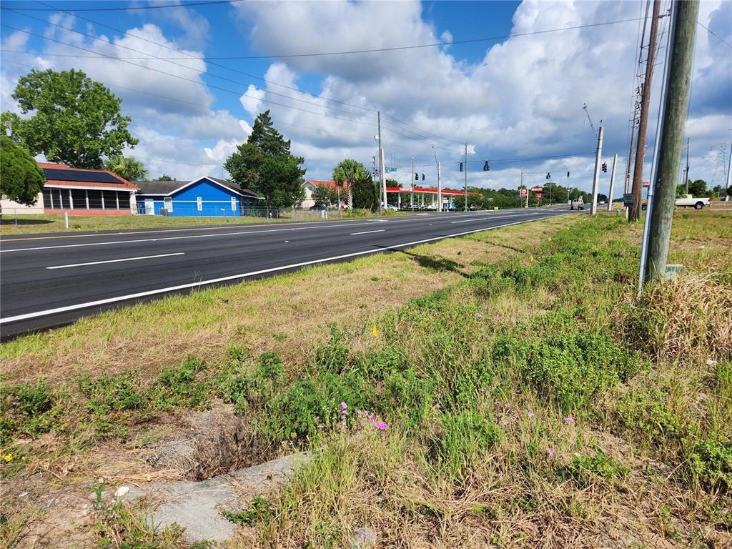 A view of a paved road with a grassy shoulder and a gas station nearby — 7013 SE MARICAMP ROAD, OCALA, FL