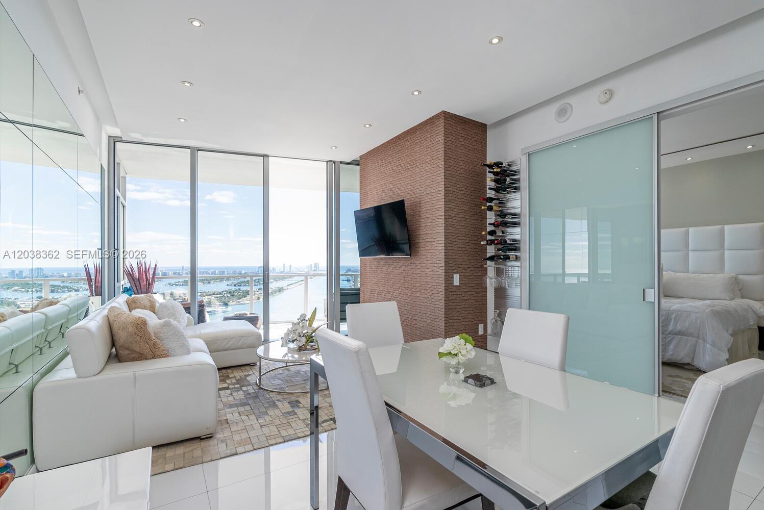 A modern living and dining area features a white sofa, glass table, and balcony view — 1100 Biscayne Blvd # 4103, Miami FL 33132, MIAMI, FL