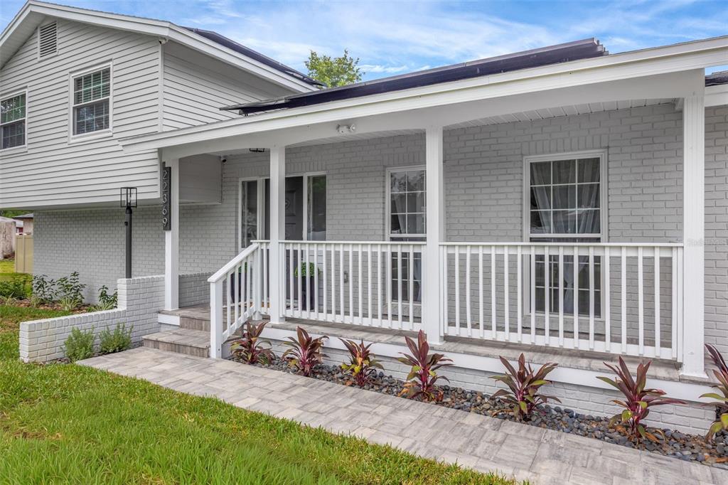 A gray brick house features a white covered porch, a stone walkway, and landscaping — 22369 SOUTHSHORE DRIVE, LAND O LAKES, FL