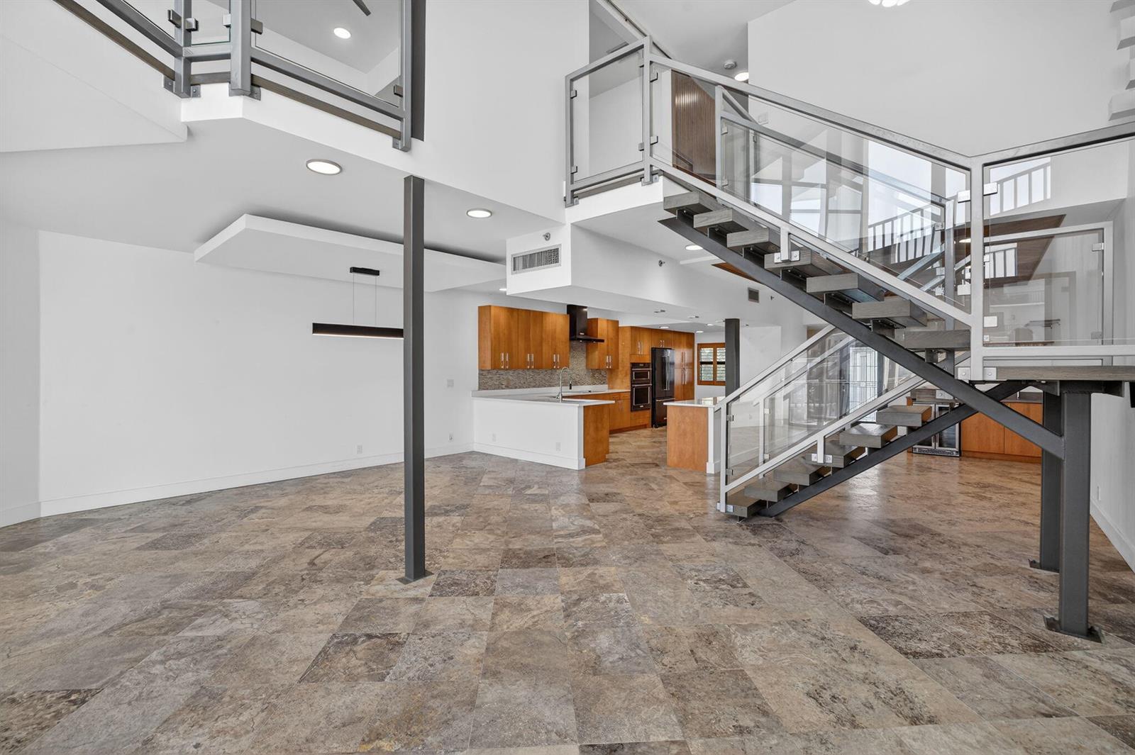 An open-concept living area features a modern staircase with glass railings and stone tile flooring — 1035 S Federal Highway # 402, Delray Beach FL 33483, DELRAY BEACH, FL