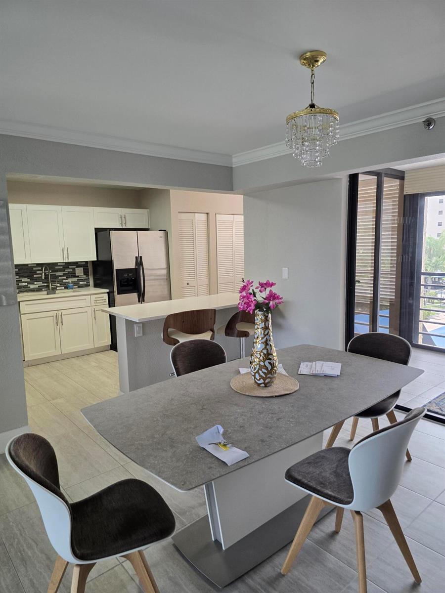 A dining area with a stone-topped table and chairs sits adjacent to a white kitchen — 7580 Regency Lake Drive # 402, Boca Raton FL 33433, BOCA RATON, FL