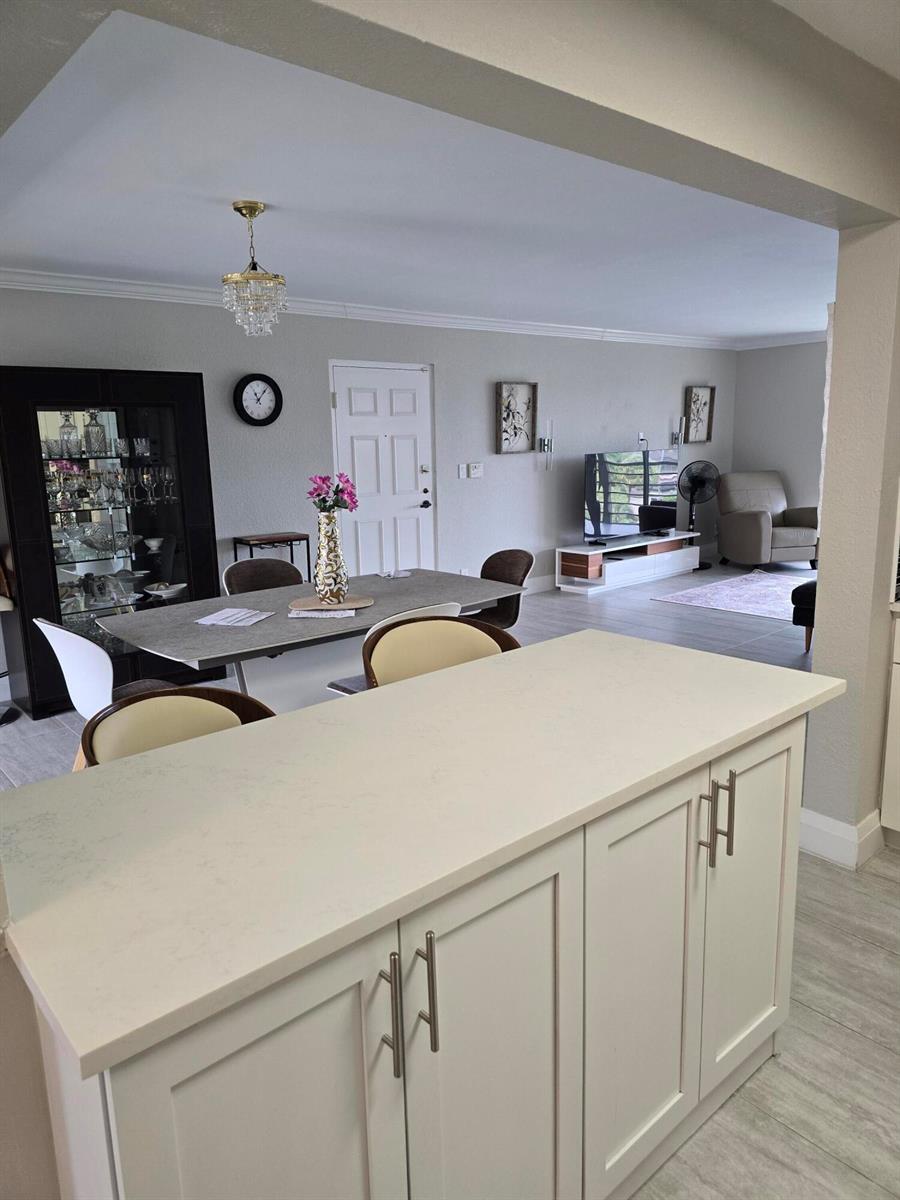 A kitchen island with white cabinets overlooks an open-concept dining area and living room — 7580 Regency Lake Drive # 402, Boca Raton FL 33433, BOCA RATON, FL