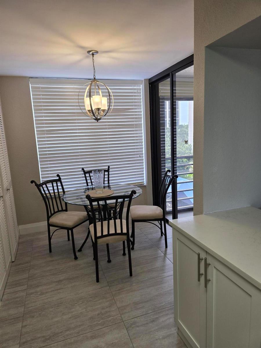 A dining area features a glass-topped table, three chairs, a pendant light, and tile flooring — 7580 Regency Lake Drive # 402, Boca Raton FL 33433, BOCA RATON, FL
