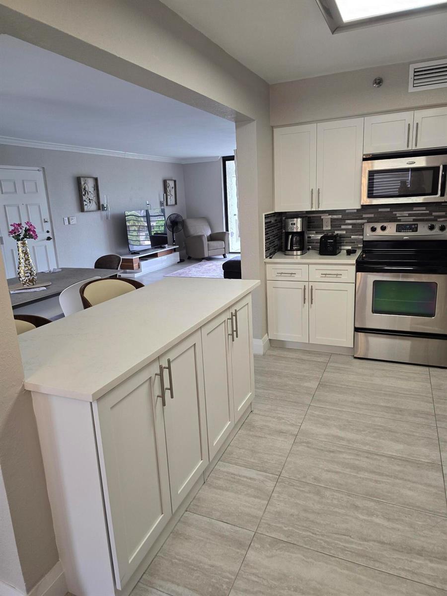 A kitchen with white cabinets, stainless steel appliances, and a breakfast bar overlooks the living area — 7580 Regency Lake Drive # 402, Boca Raton FL 33433, BOCA RATON, FL