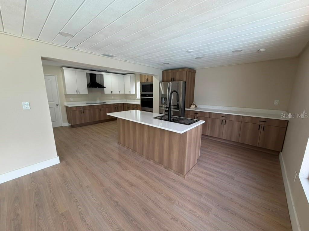 A kitchen features wood-toned lower cabinets, white upper cabinets, a central island, and light flooring — 1822 BANYAN TREE DRIVE, EDGEWATER, FL
