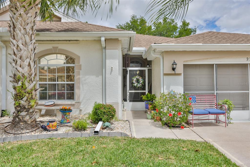 The exterior of a single-story home features a palm tree, a front porch, and a bench — 2305 OLIVE BRANCH DRIVE, SUN CITY CENTER, FL