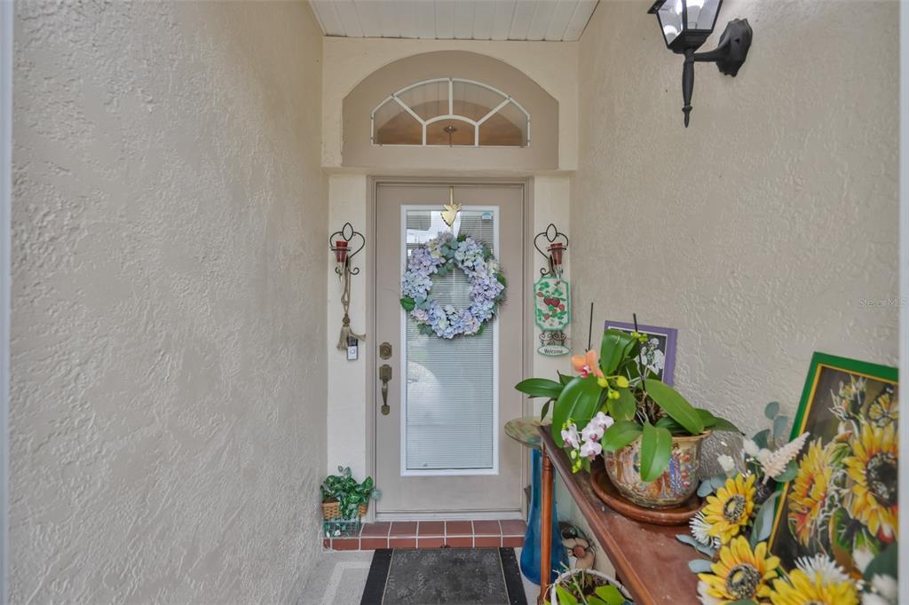 A covered entryway features a beige front door with a wreath and a transom window — 2305 OLIVE BRANCH DRIVE, SUN CITY CENTER, FL