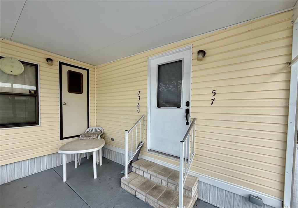 A covered porch features light yellow siding, a white front door, and stone steps — 7360 INTERNATIONAL CIRCLE, LAKE WALES, FL