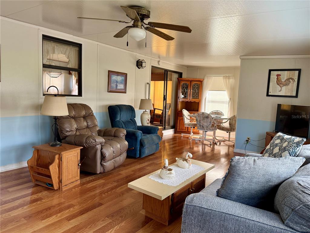 A living room features wood flooring, a ceiling fan, and a dining area in back — 7360 INTERNATIONAL CIRCLE, LAKE WALES, FL