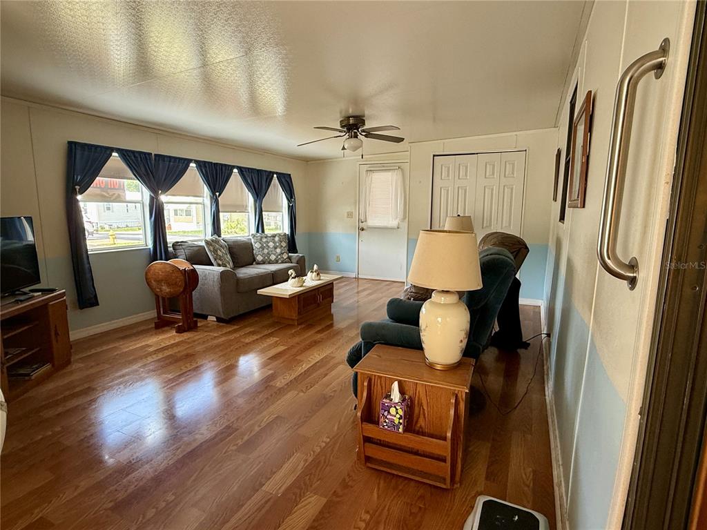 A living room features wood-look flooring, a ceiling fan, a gray sofa, and blue walls — 7360 INTERNATIONAL CIRCLE, LAKE WALES, FL
