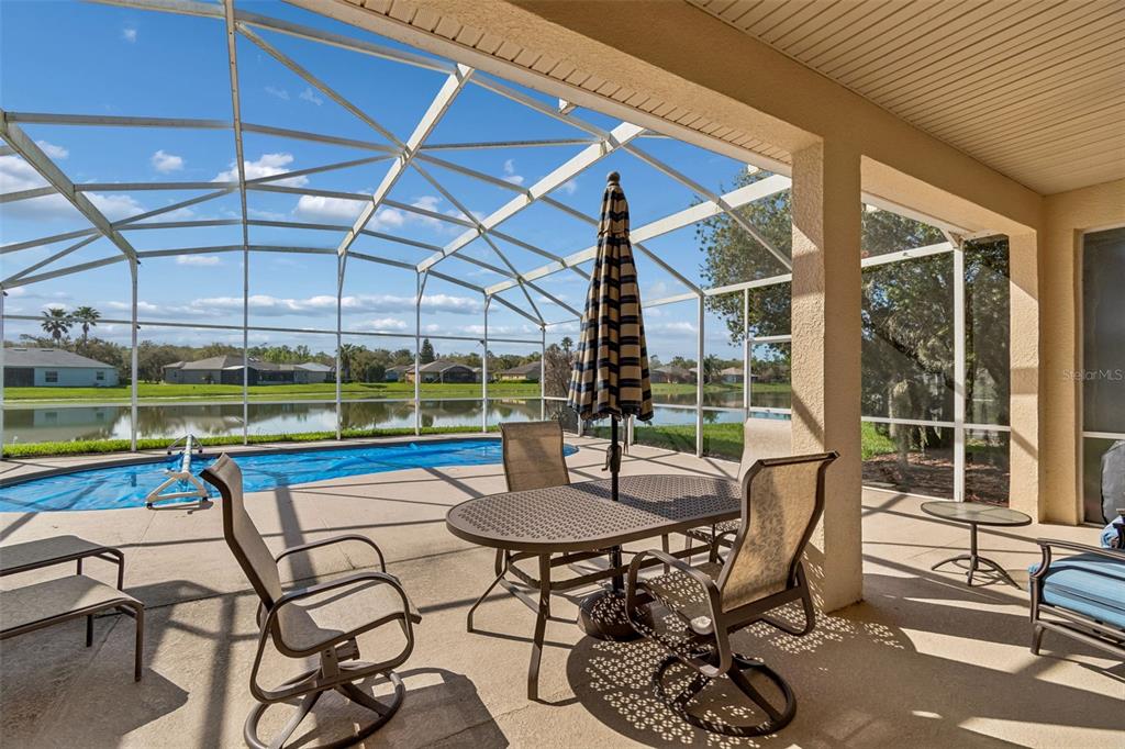 A covered patio features a screened-in pool, outdoor furniture, and a view of a lake — 813 GLENDORA ROAD, KISSIMMEE, FL