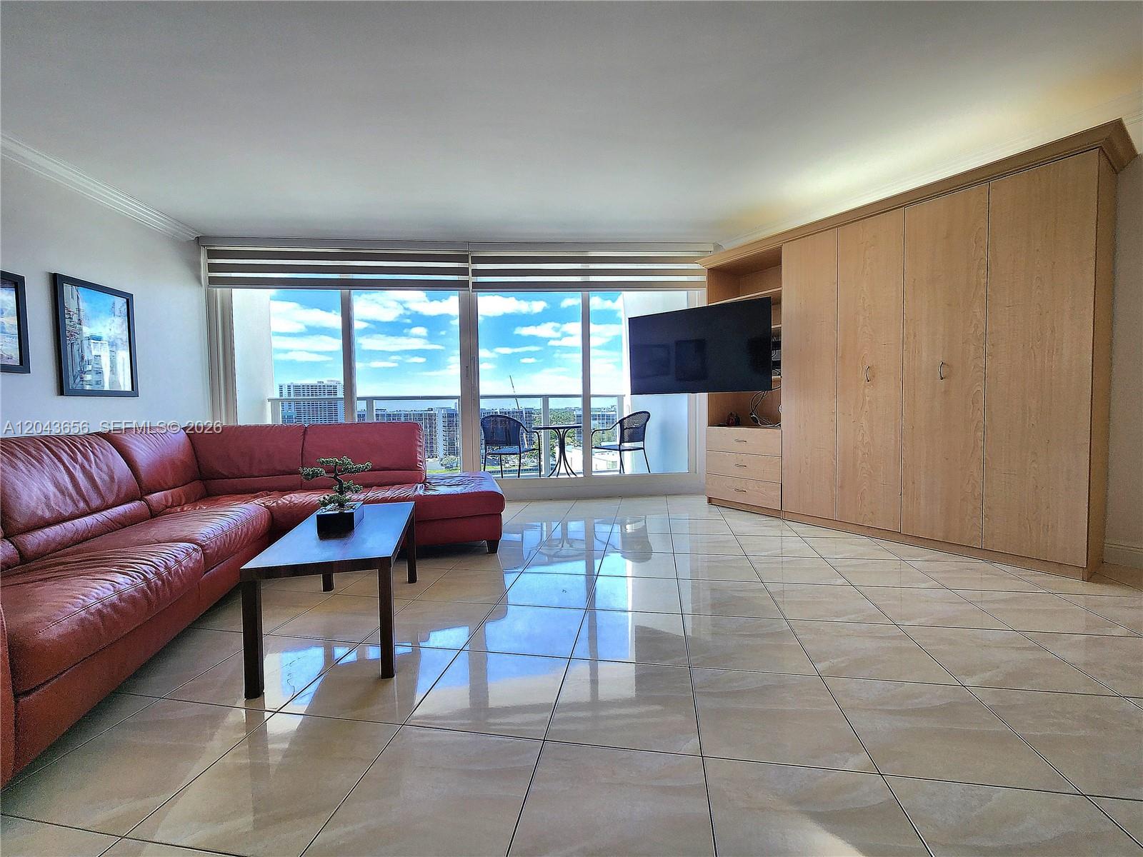 A living room features a red leather sectional, tile flooring, and a large wall unit — 3505 S Ocean Dr # 1103, Hollywood FL 33019, HOLLYWOOD, FL