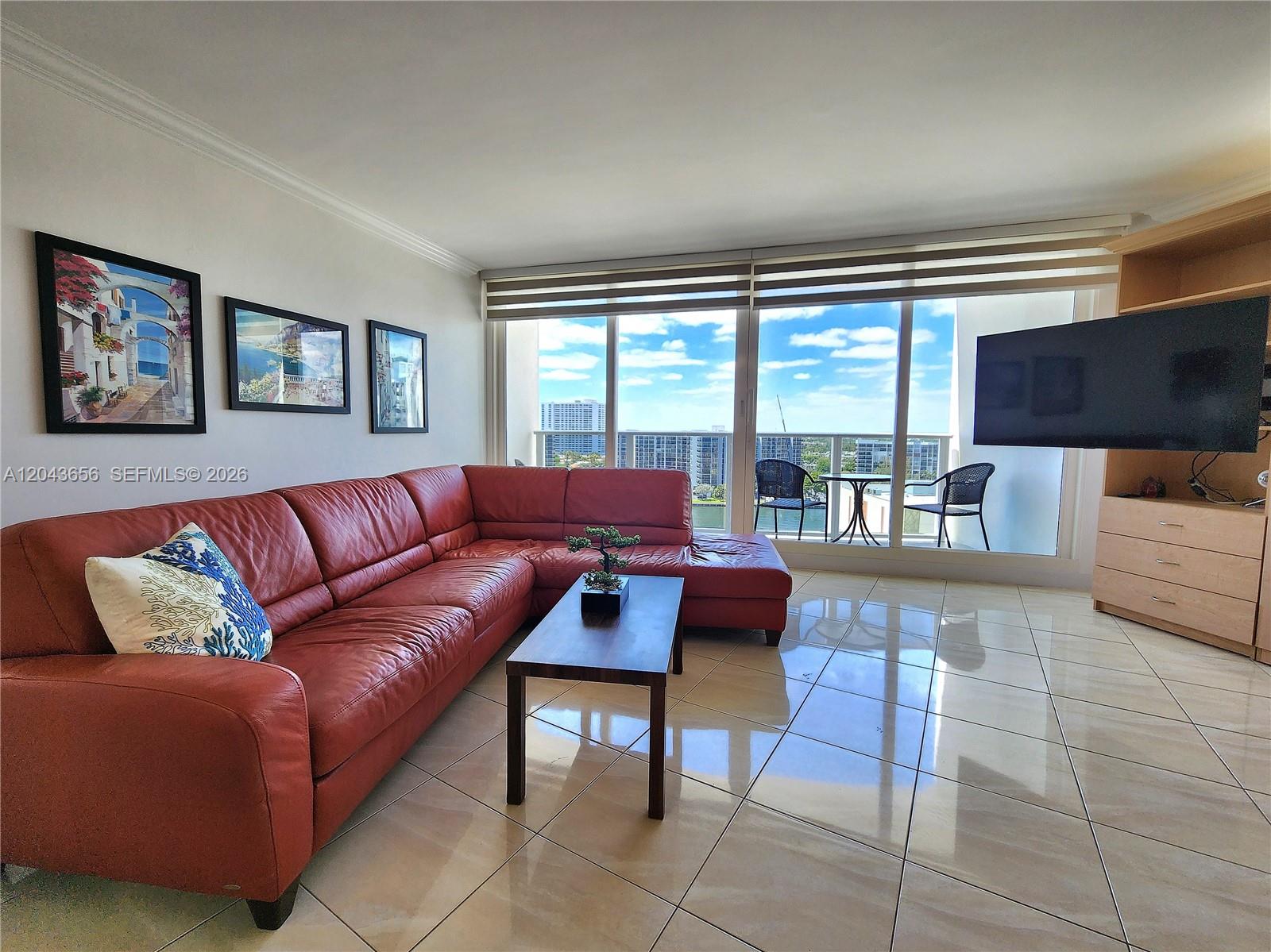 A living room features a red leather sectional, tile flooring, and a balcony with views — 3505 S Ocean Dr # 1103, Hollywood FL 33019, HOLLYWOOD, FL