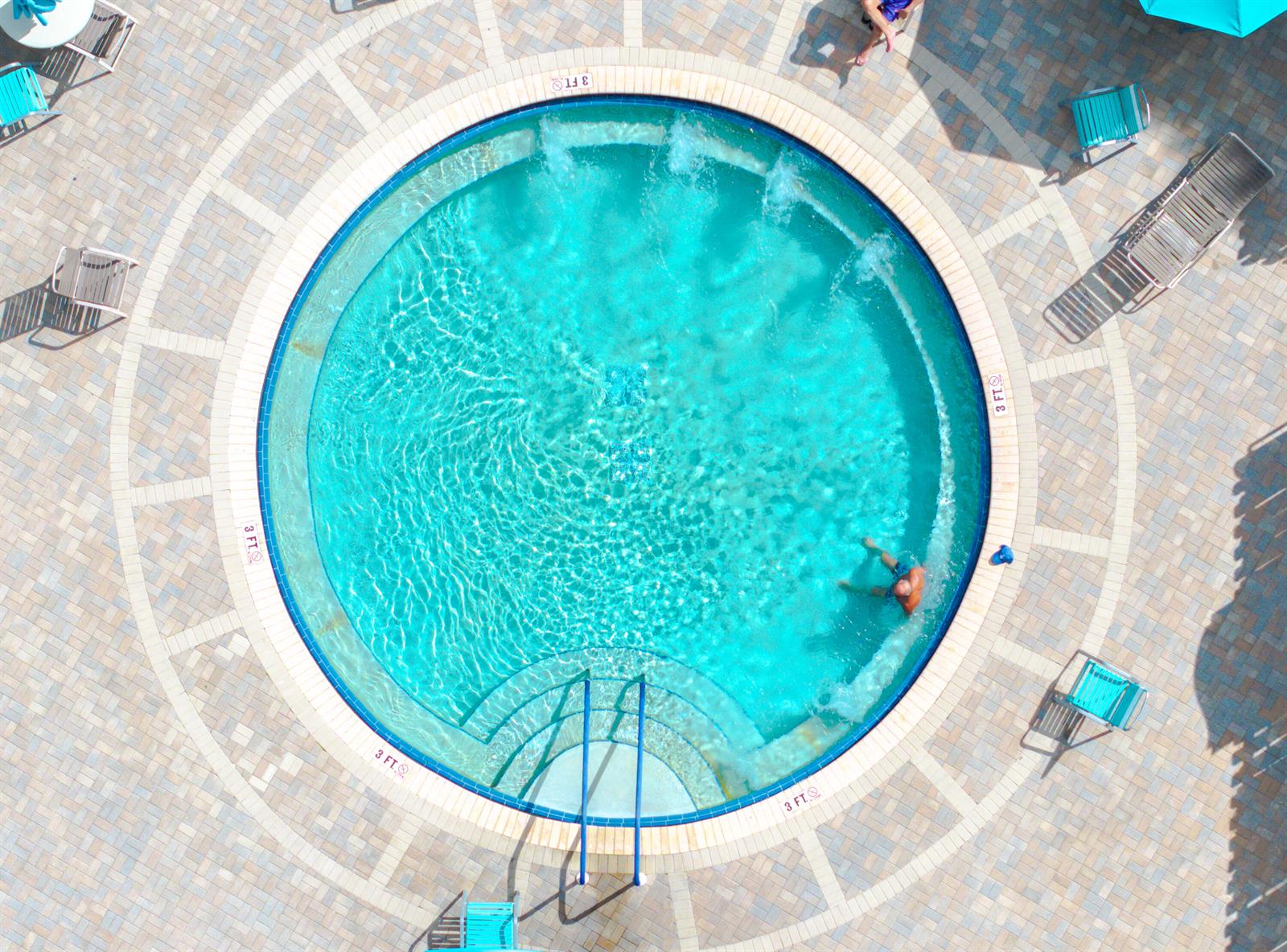 An aerial view of a circular swimming pool surrounded by a paved deck and lounge chairs — 233 Brittany E, Delray Beach FL 33446, DELRAY BEACH, FL