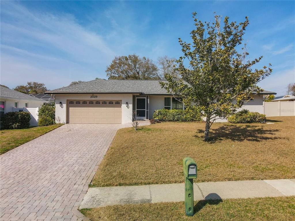 A single-story house with a paved driveway, a tan garage door, and a front lawn — 2029 SPANISH PINES DRIVE, DUNEDIN, FL