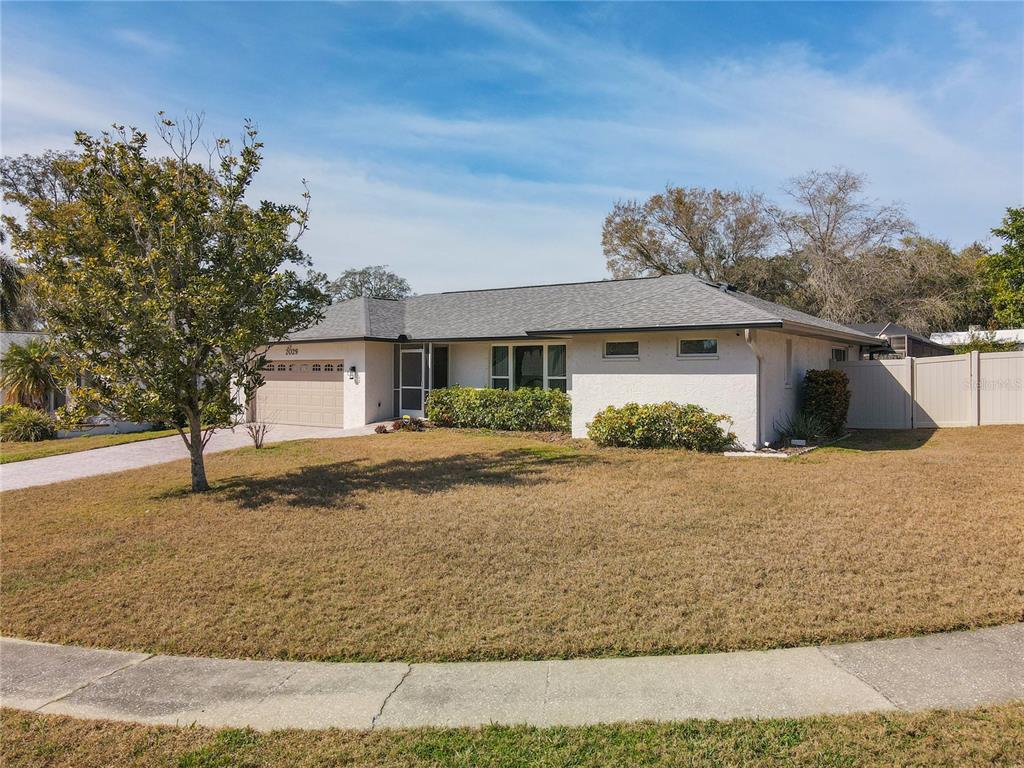 A single-story house with a tan stucco exterior, a gray shingled roof, and a front lawn — 2029 SPANISH PINES DRIVE, DUNEDIN, FL