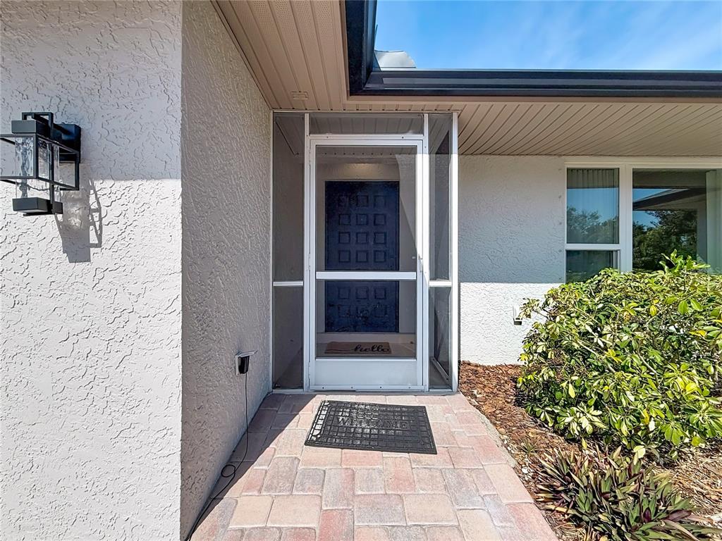 A paved walkway leads to a front entrance with a screen door and dark door — 2029 SPANISH PINES DRIVE, DUNEDIN, FL