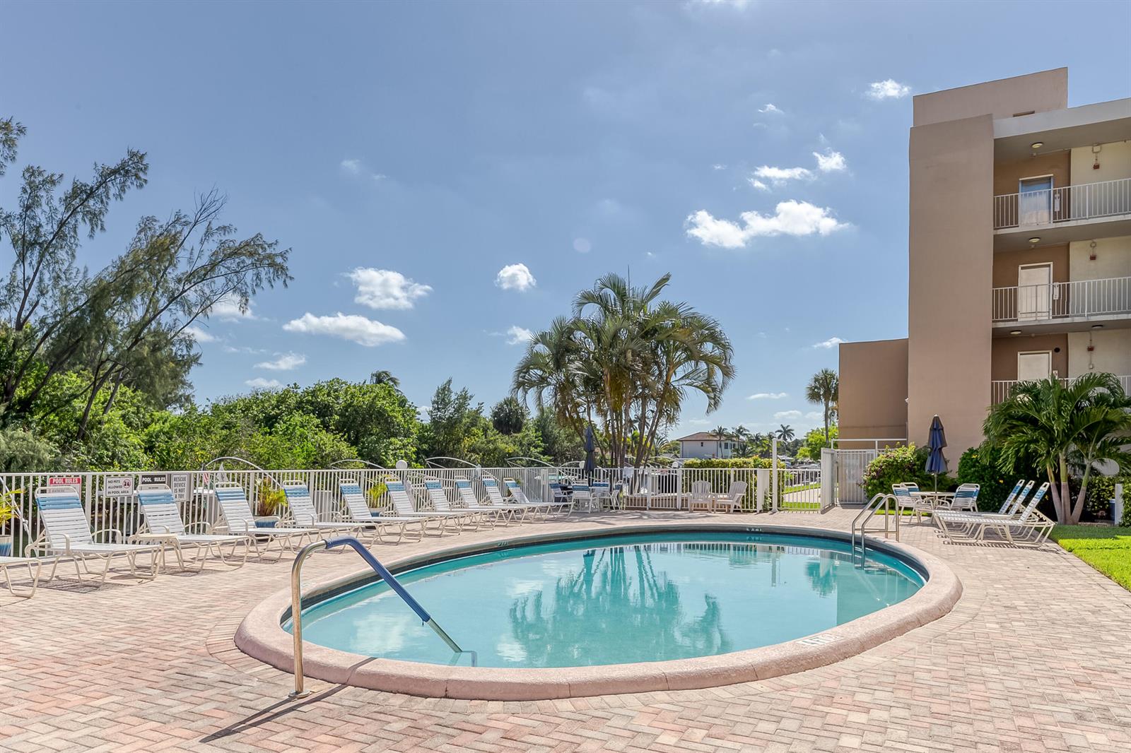An oval swimming pool is surrounded by a brick patio, lounge chairs, and palm trees — 2850 NE 14th St Causeway # 308b, Pompano Beach FL 33062, POMPANO BEACH, FL