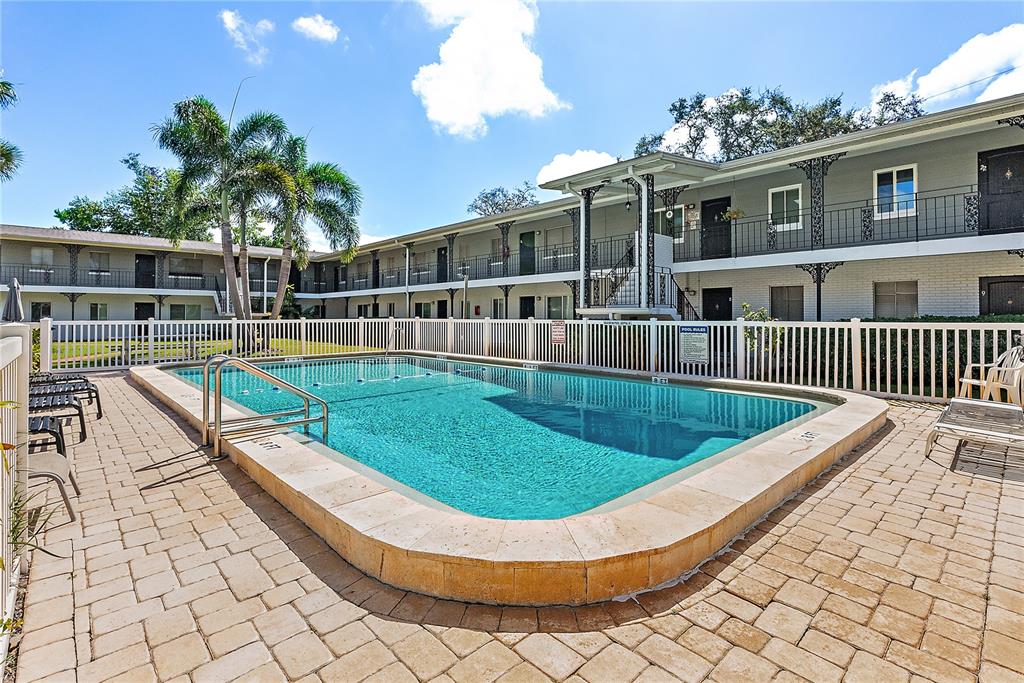 A rectangular swimming pool with a stone deck sits in front of a two-story apartment building — 6266 1ST AVENUE S UNIT 29, ST PETERSBURG, FL