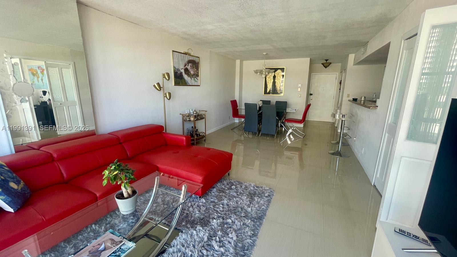A living and dining area features a red sectional sofa, glass coffee table, and tile flooring — 2017 OCEAN DR # 405W, Hallandale Beach FL 33009, HALLANDALE BEACH, FL