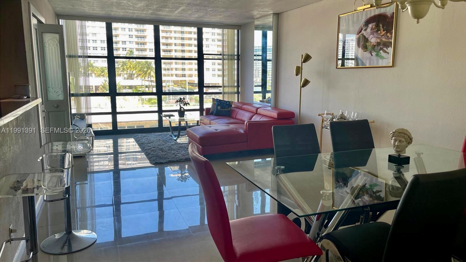 A living and dining area features a red sofa, glass table, and floor-to-ceiling windows — 2017 OCEAN DR # 405W, Hallandale Beach FL 33009, HALLANDALE BEACH, FL